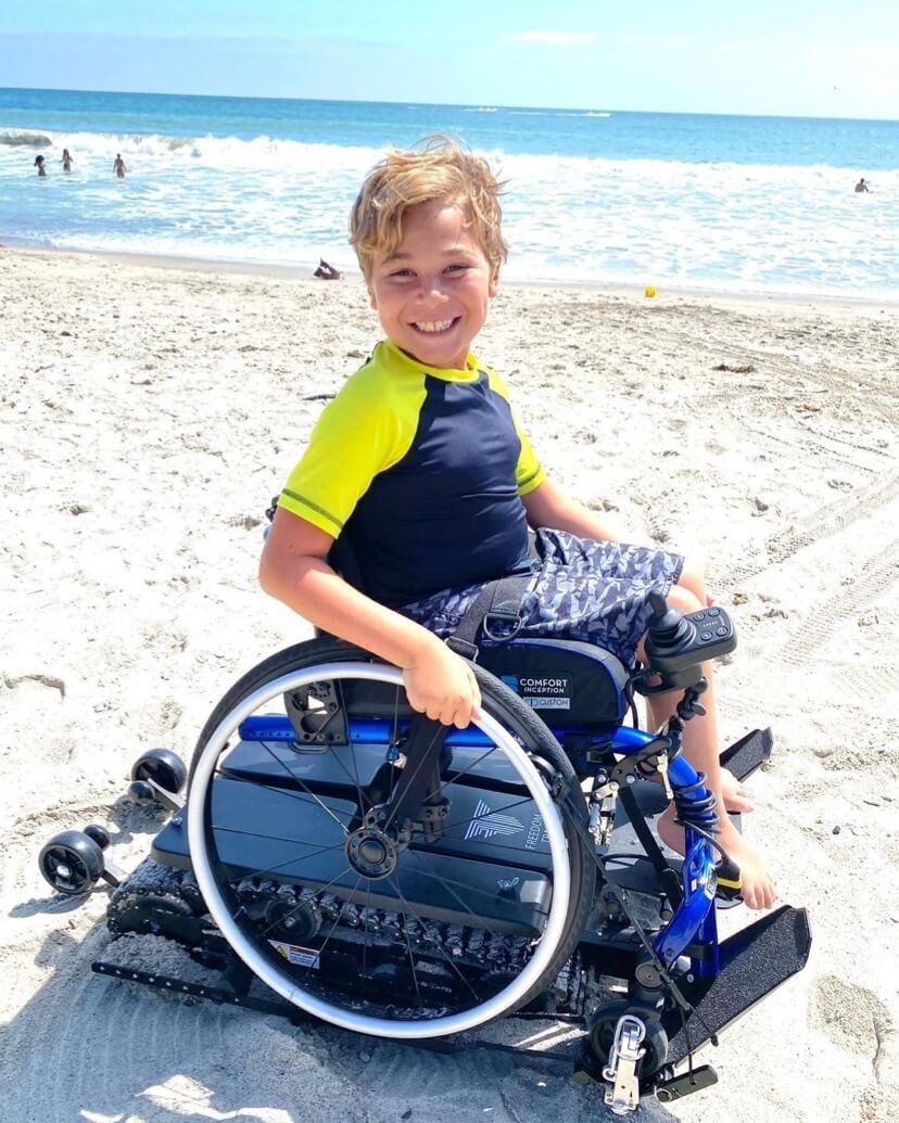 Happy boy on sand in wheelchair